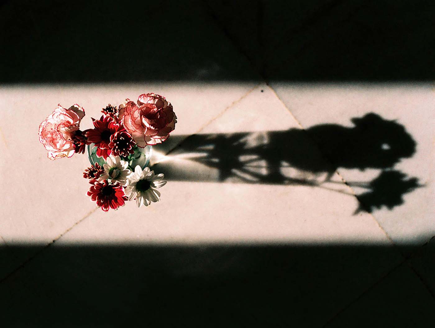 Flower bouquet and shadow in dramatic morning light on marble floor