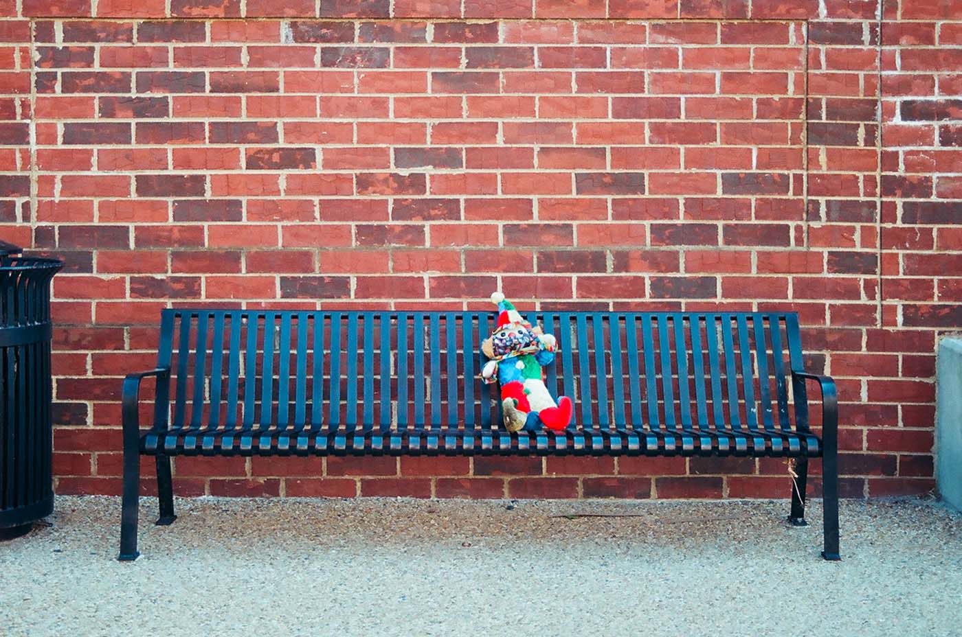 Clown toy sitting on bench with brick wall behind